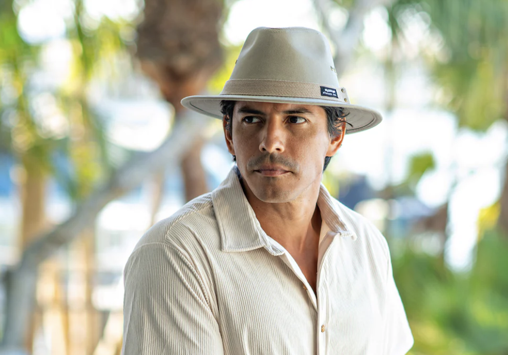 Stern looking man wearing a off-white button up shirt and light gray hat