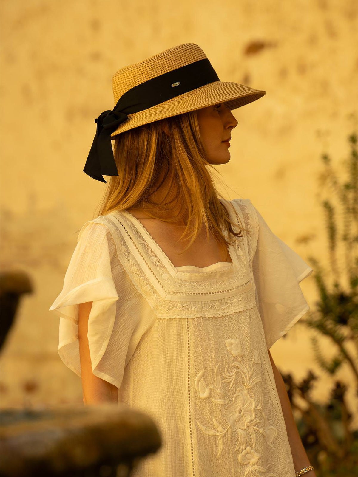 Woman wearing a straw hat with a black ribbon against a warm, blurred background