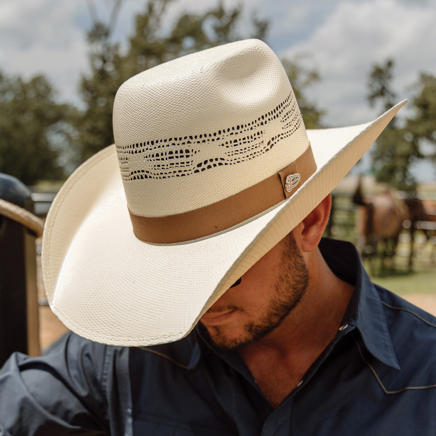 Man wearing a beige cowboy hat with a brown band outdoors