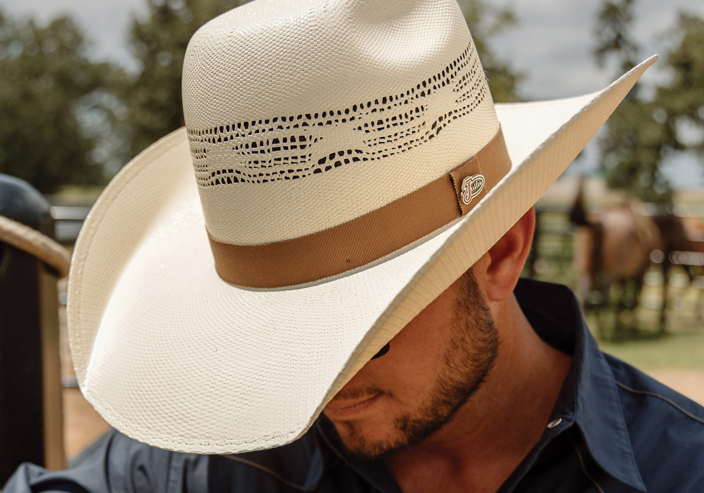 Man wearing a beige cowboy hat with a brown band outdoors